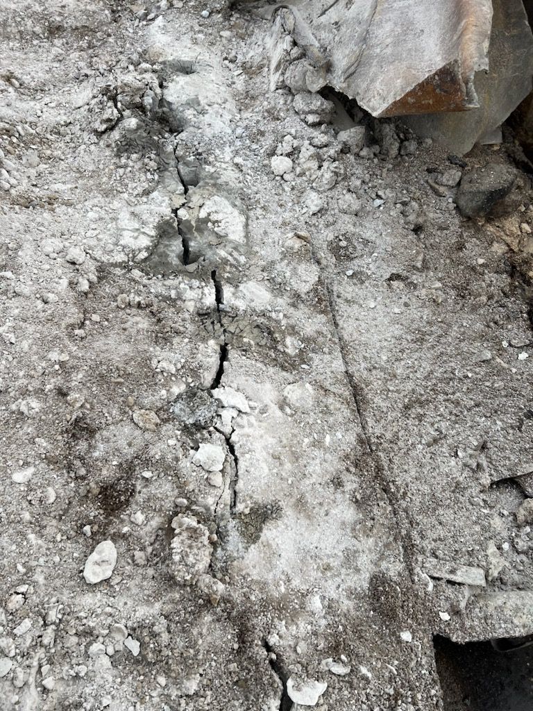 Close-up of a cracked, gray surface covered in light-colored residue. A dark crack runs vertically.