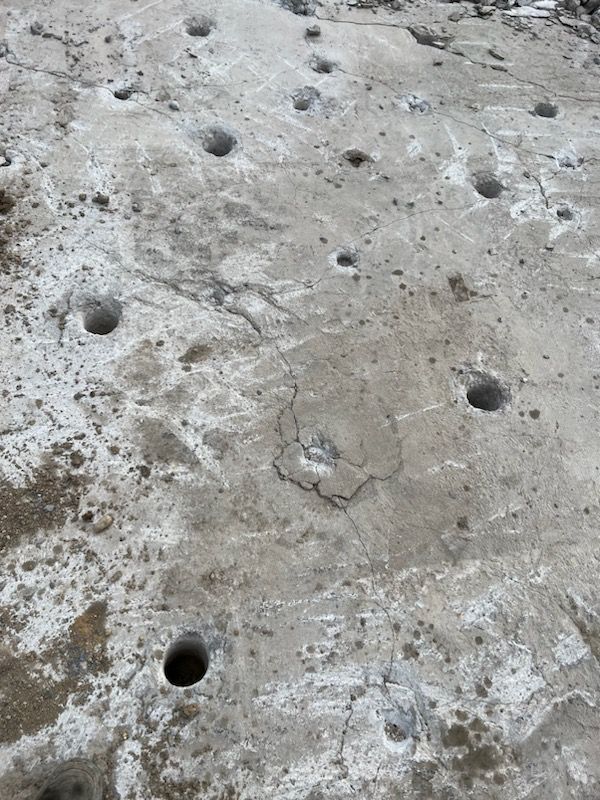 Gray concrete surface with multiple drilled holes and cracks.