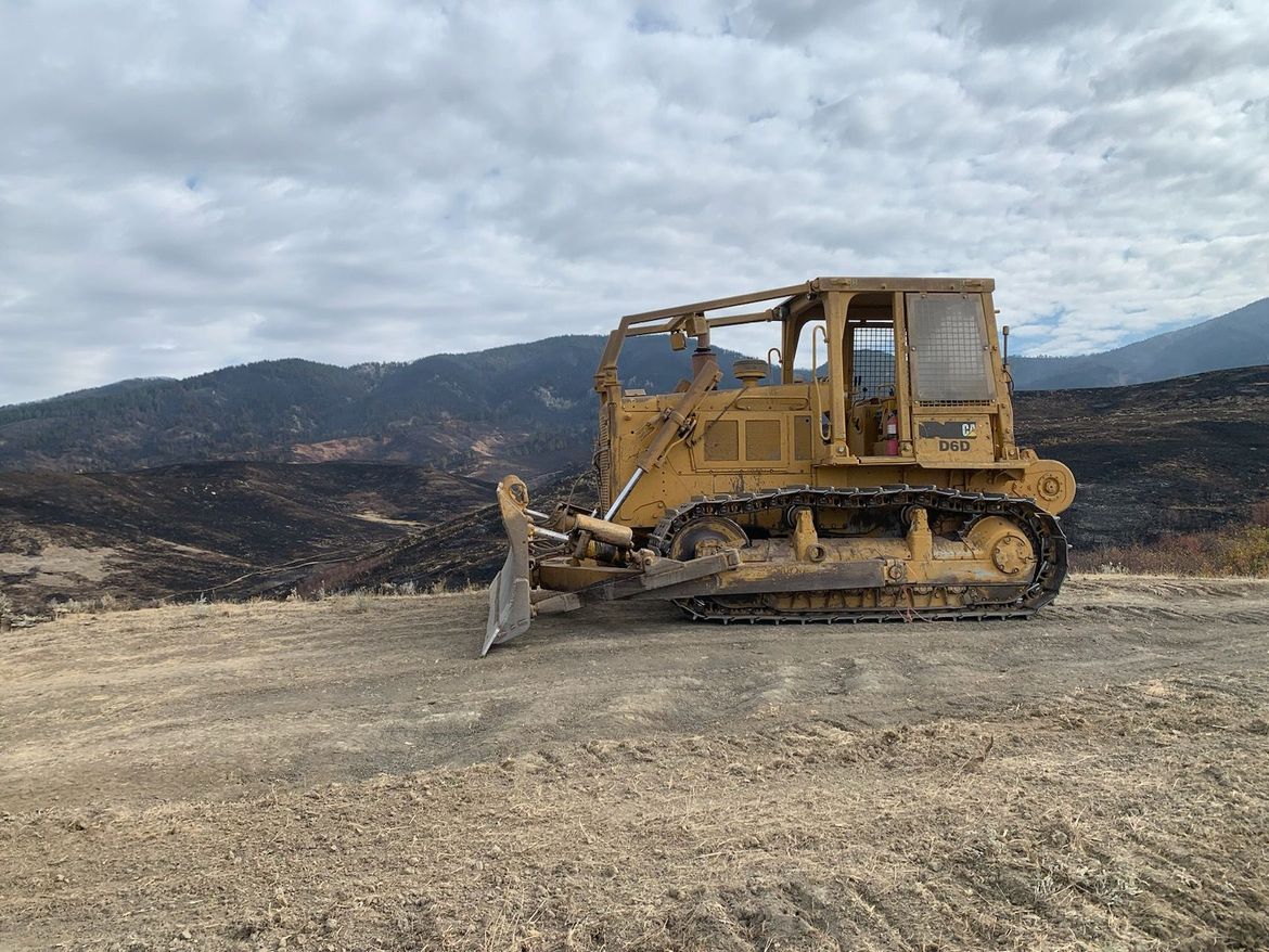 Yellow bulldozer parked on gravel road, charred landscape behind.