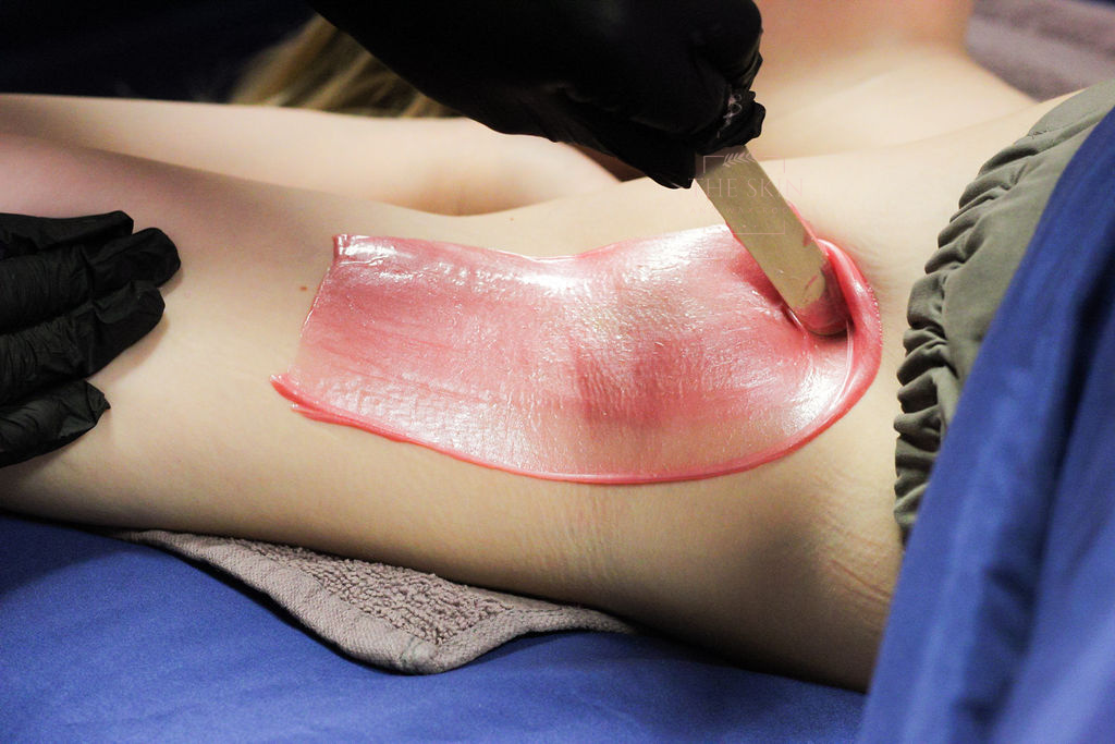 A woman in a red bra is getting her armpit waxed.