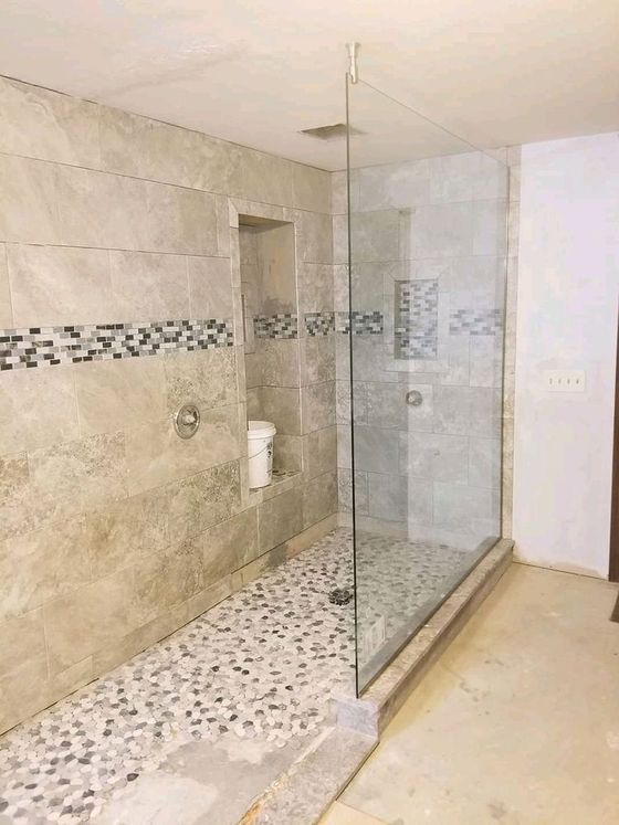 Modern bathroom with glass walk-in shower, beige tile walls, and pebble mosaic floor.