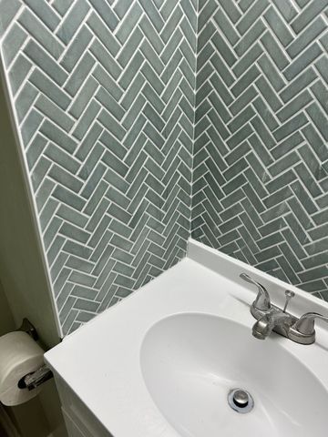 Small bathroom sink beside gray herringbone tile wall and mounted toilet paper holder