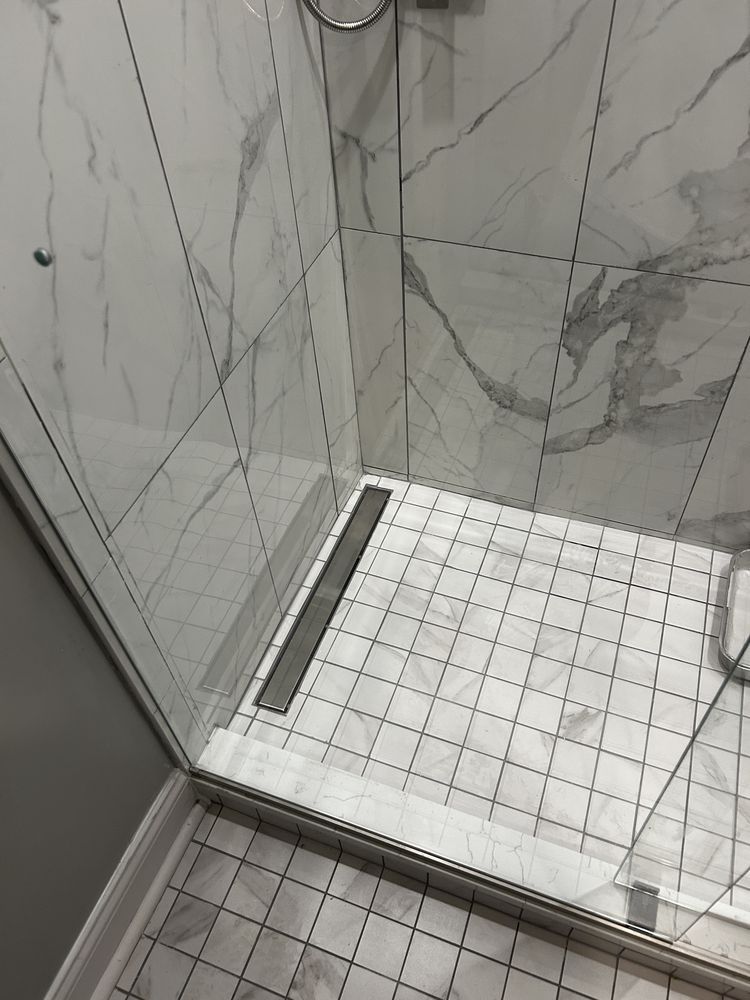 Tiled shower stall with glass door, white floor tiles, and gray marble-pattern wall tiles.