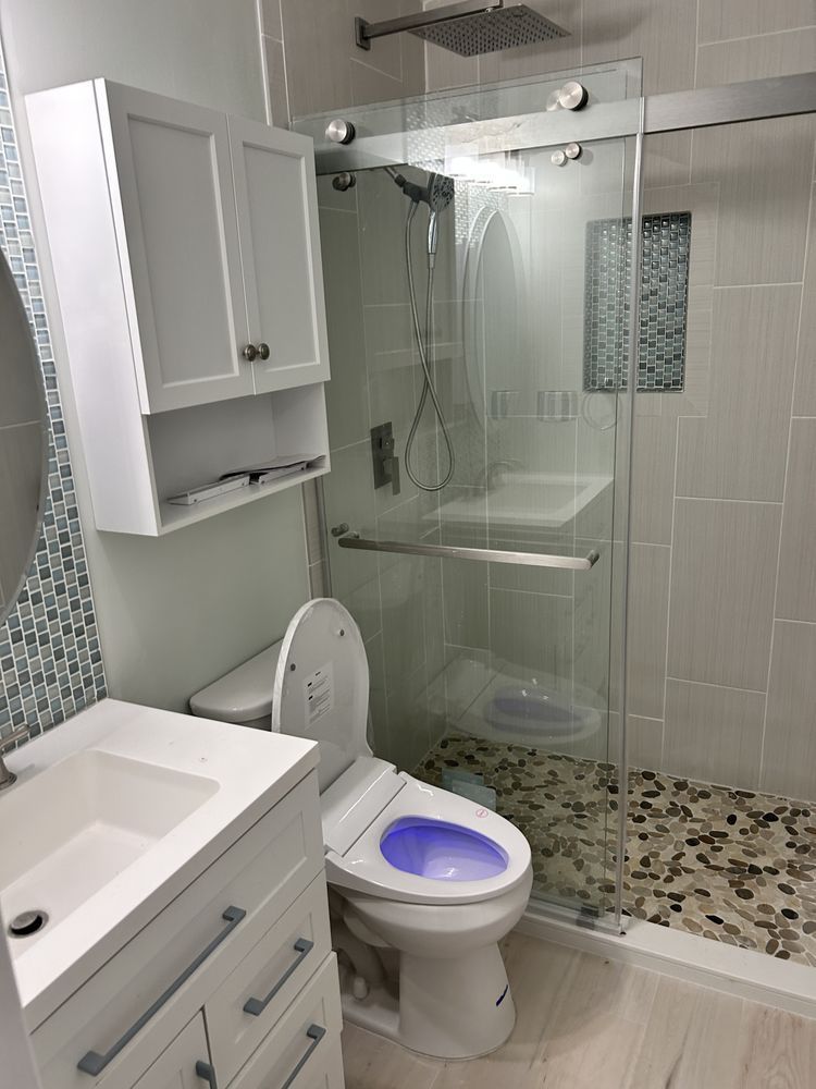 Small bathroom with white vanity, toilet, glass shower, and pebble-style shower floor.