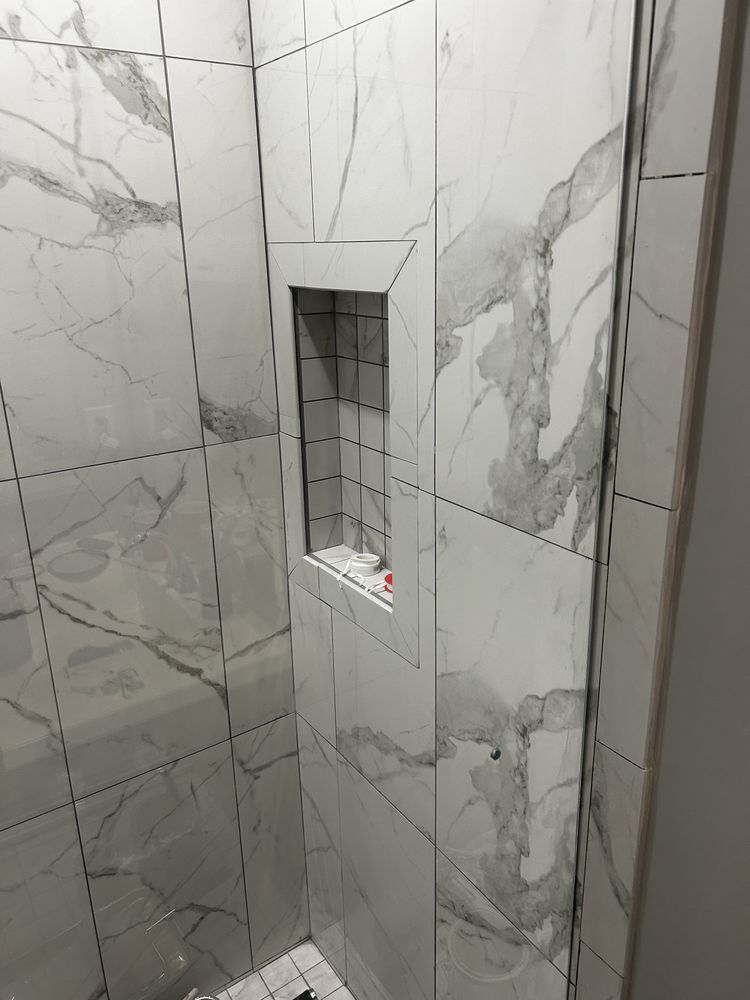 White marble-tiled shower wall with a recessed niche and small gray tile inset