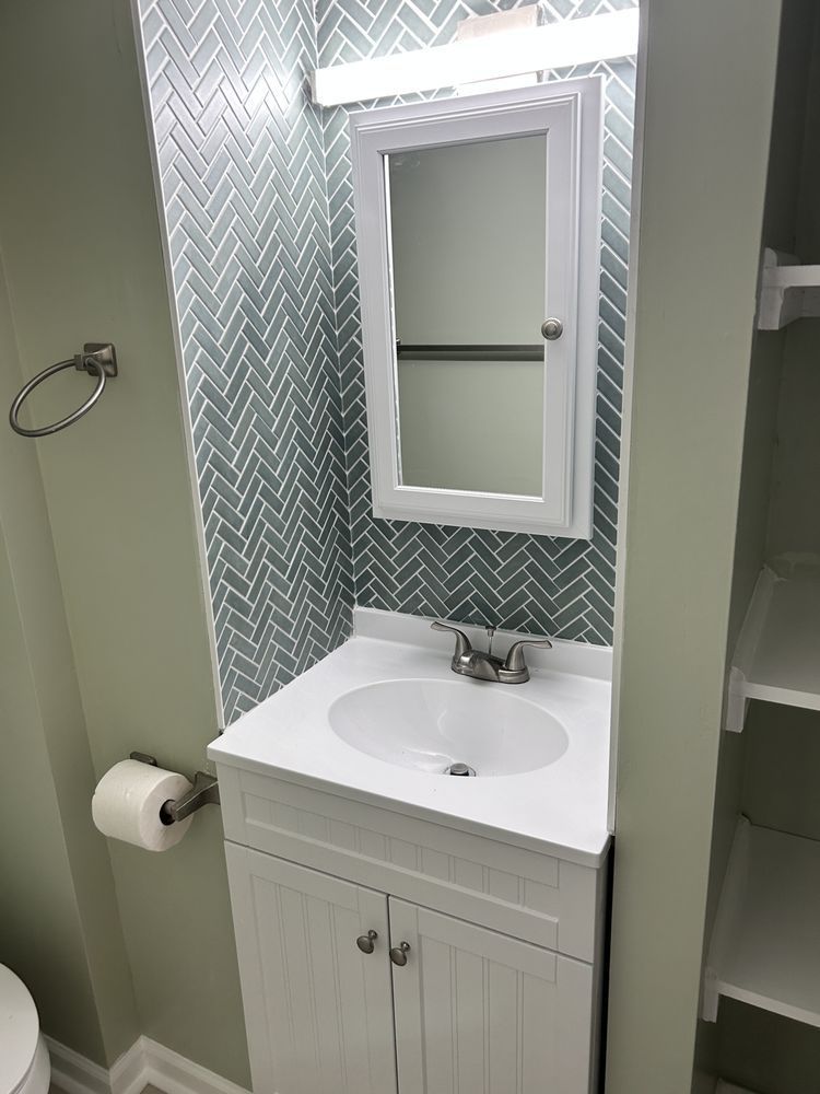 Small bathroom vanity with white sink, mirror, and teal patterned backsplash beside a toilet paper holder.