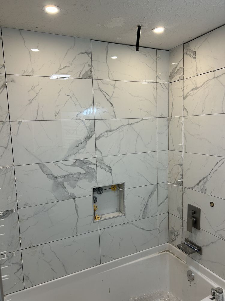 Bathroom with marble-pattern tile wall, bathtub, and unfinished wall opening above the tub.