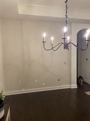 Empty beige dining room with dark wood floors and a black chandelier lit by candles