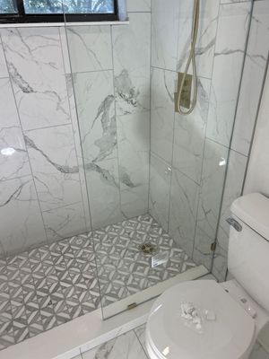 Modern white-tiled bathroom shower with patterned floor and toilet in foreground