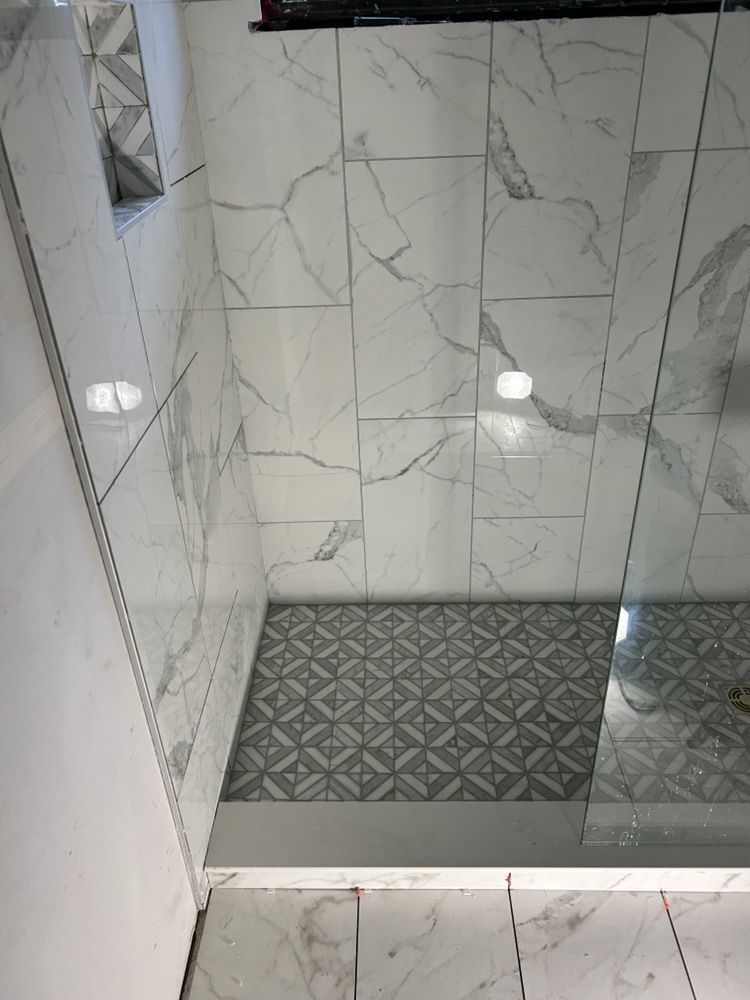 Small tiled shower with marble-pattern walls and a gray patterned floor drain area.