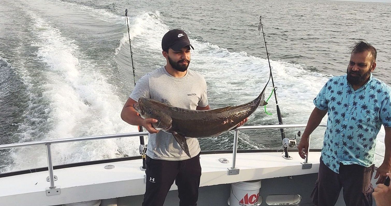 Two men are standing on a boat holding a large fish.