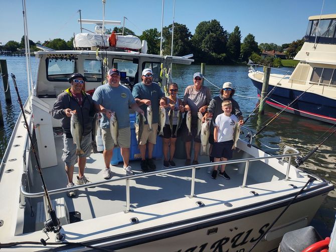 A group of people are standing in the boat's stern holding fish.