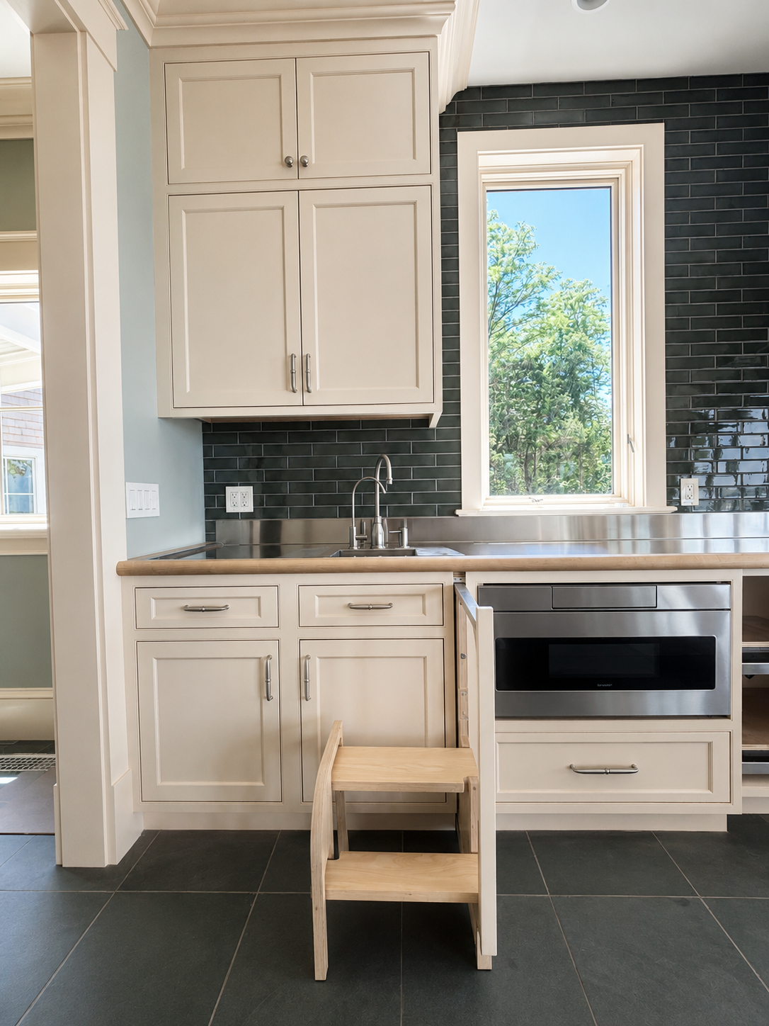 Bright kitchen with white cabinets, black tile backsplash, window, built-in oven, and small stool on the floor