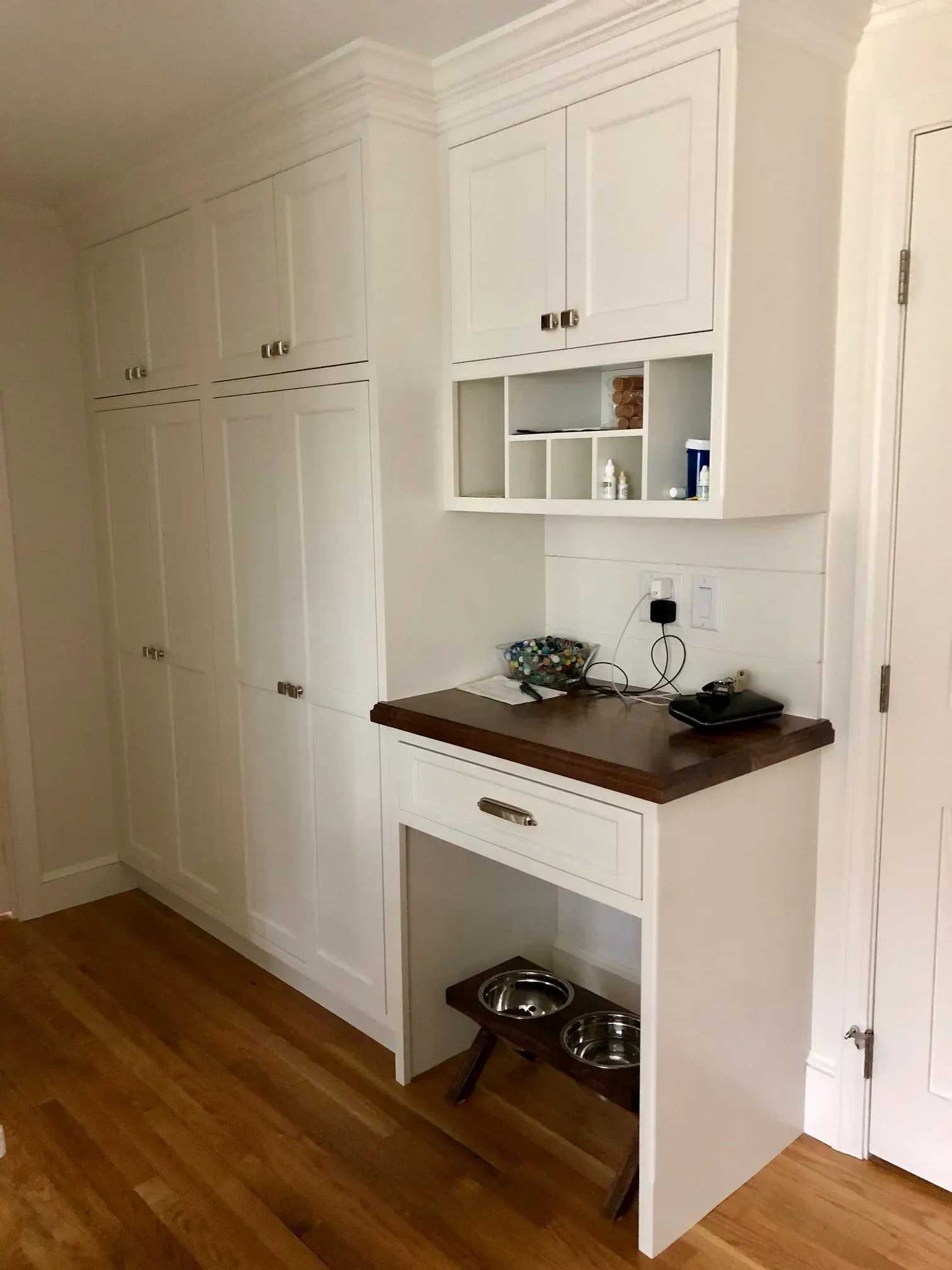 White cabinets and countertop with dog bowls, set in a wood-floored corner.
