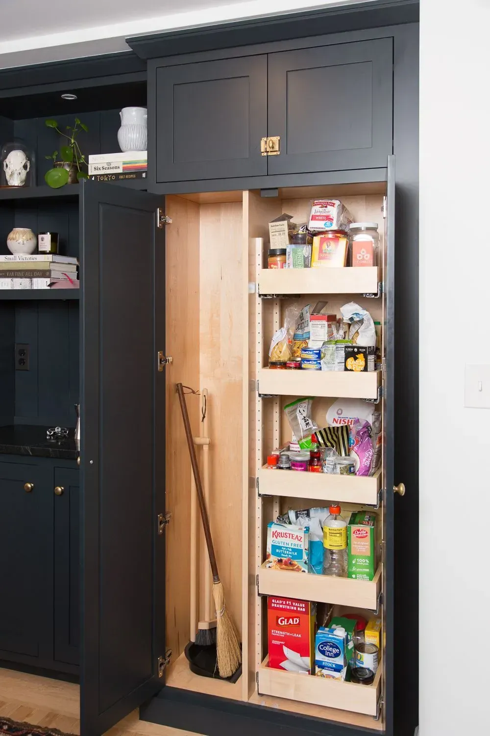 Dark blue pantry with pull-out shelves stocked with food items and broom.