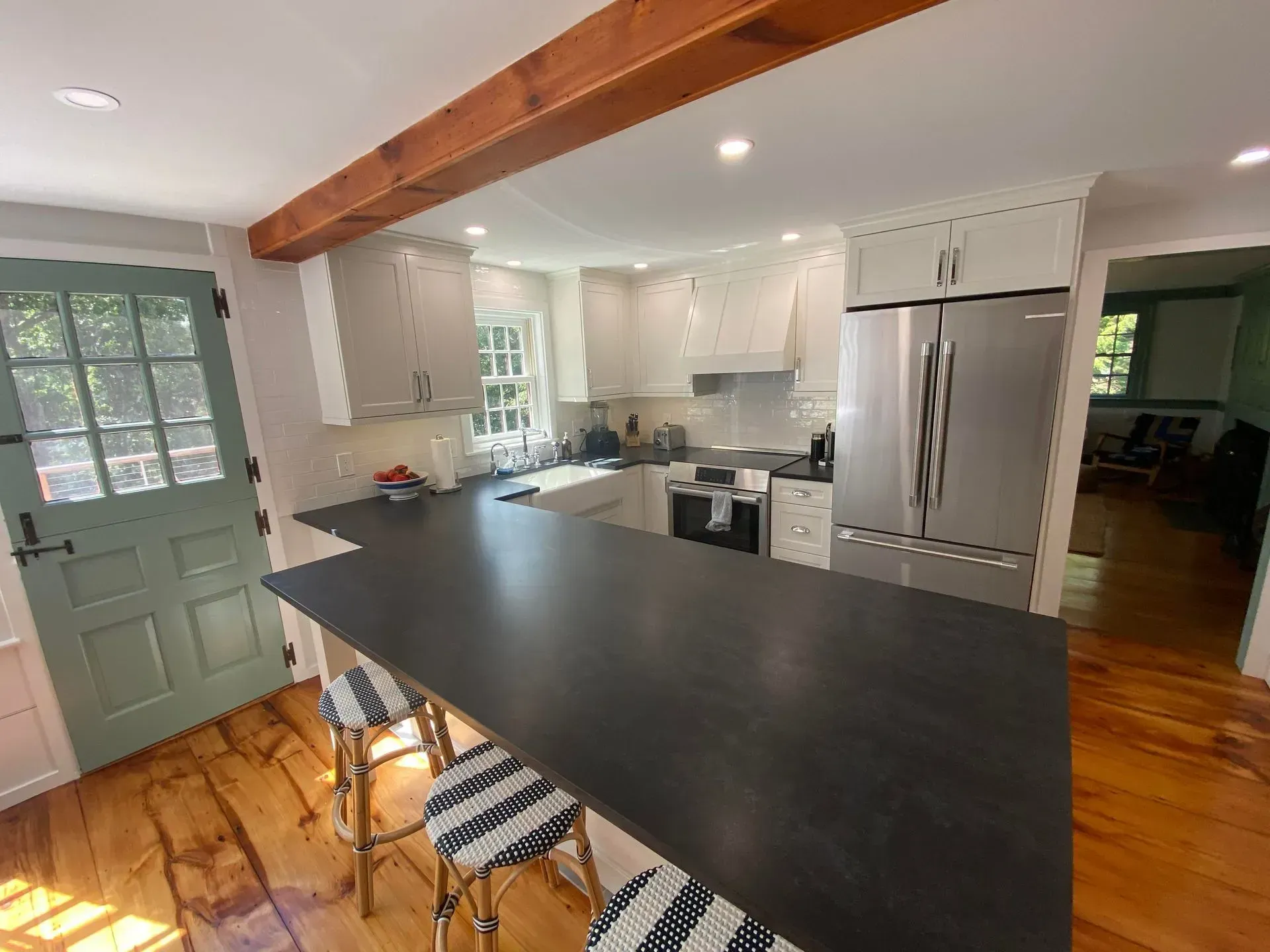 Kitchen with light gray cabinets, dark countertop, wooden floors and door, and a stainless steel refrigerator.