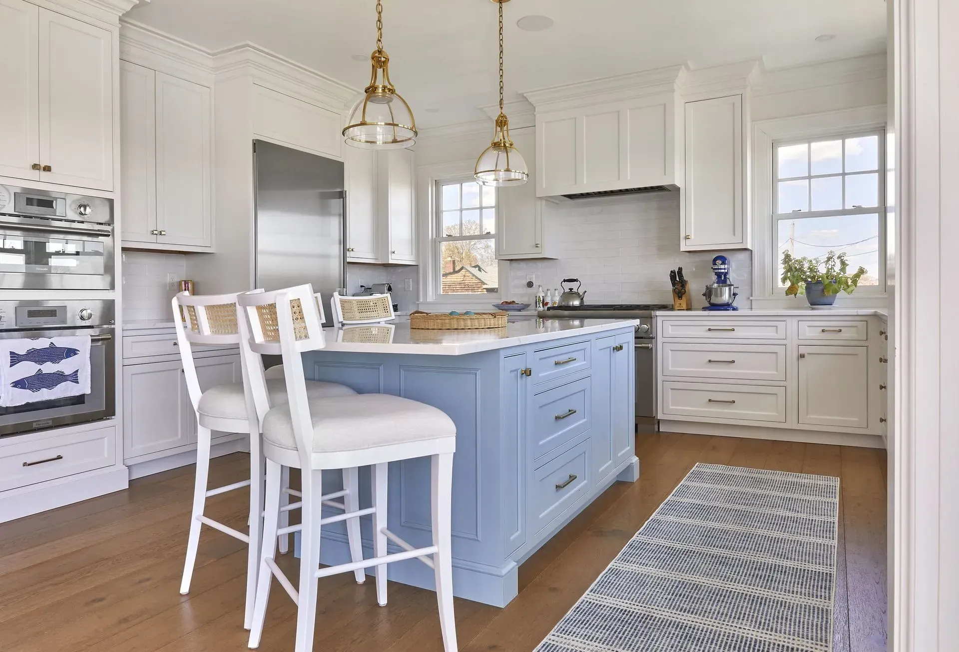Blue and white kitchen with island, stainless steel appliances, and two barstools.