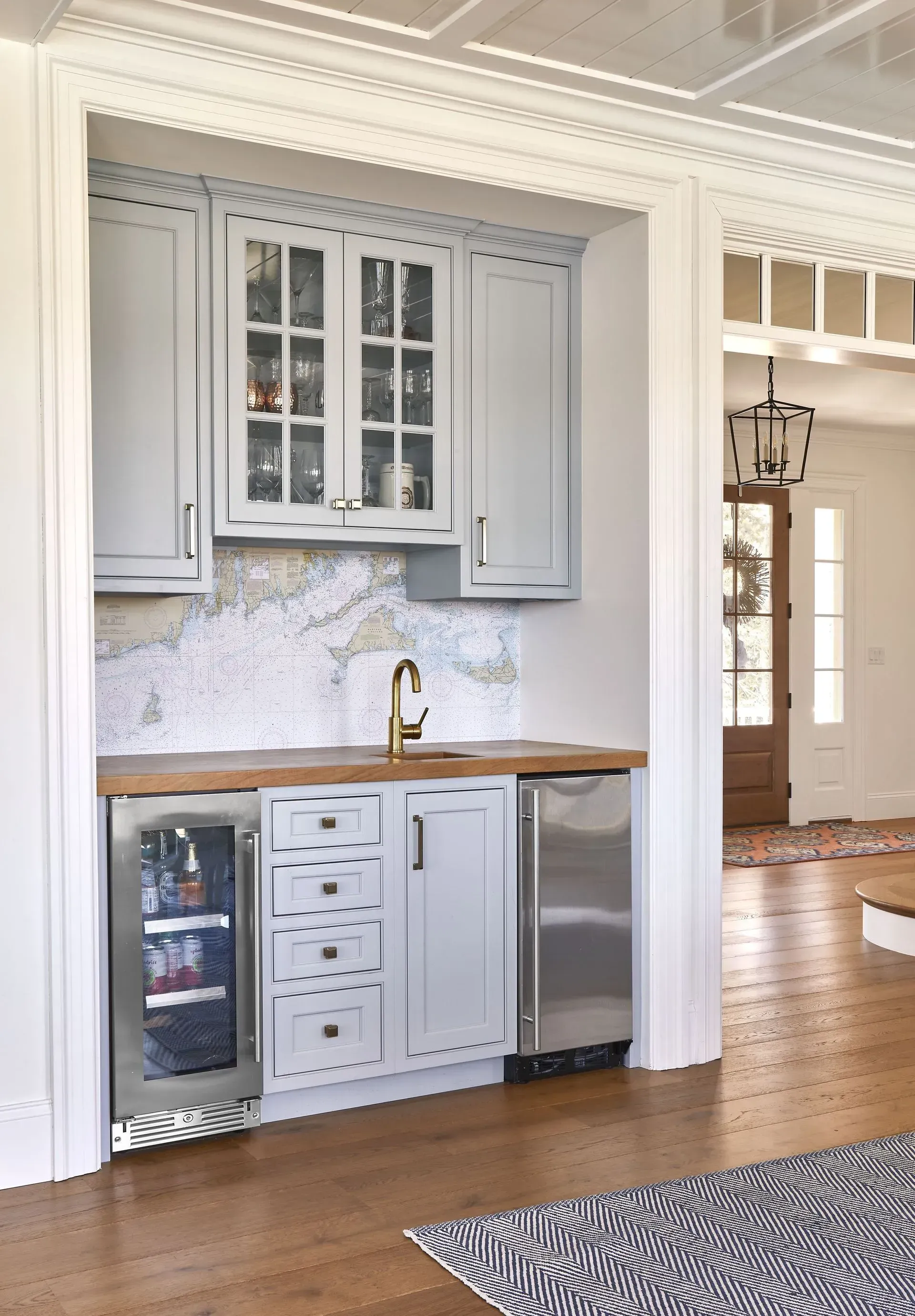 Built-in home bar with light blue cabinets, wooden countertop, and gold faucet. Includes a wine fridge.