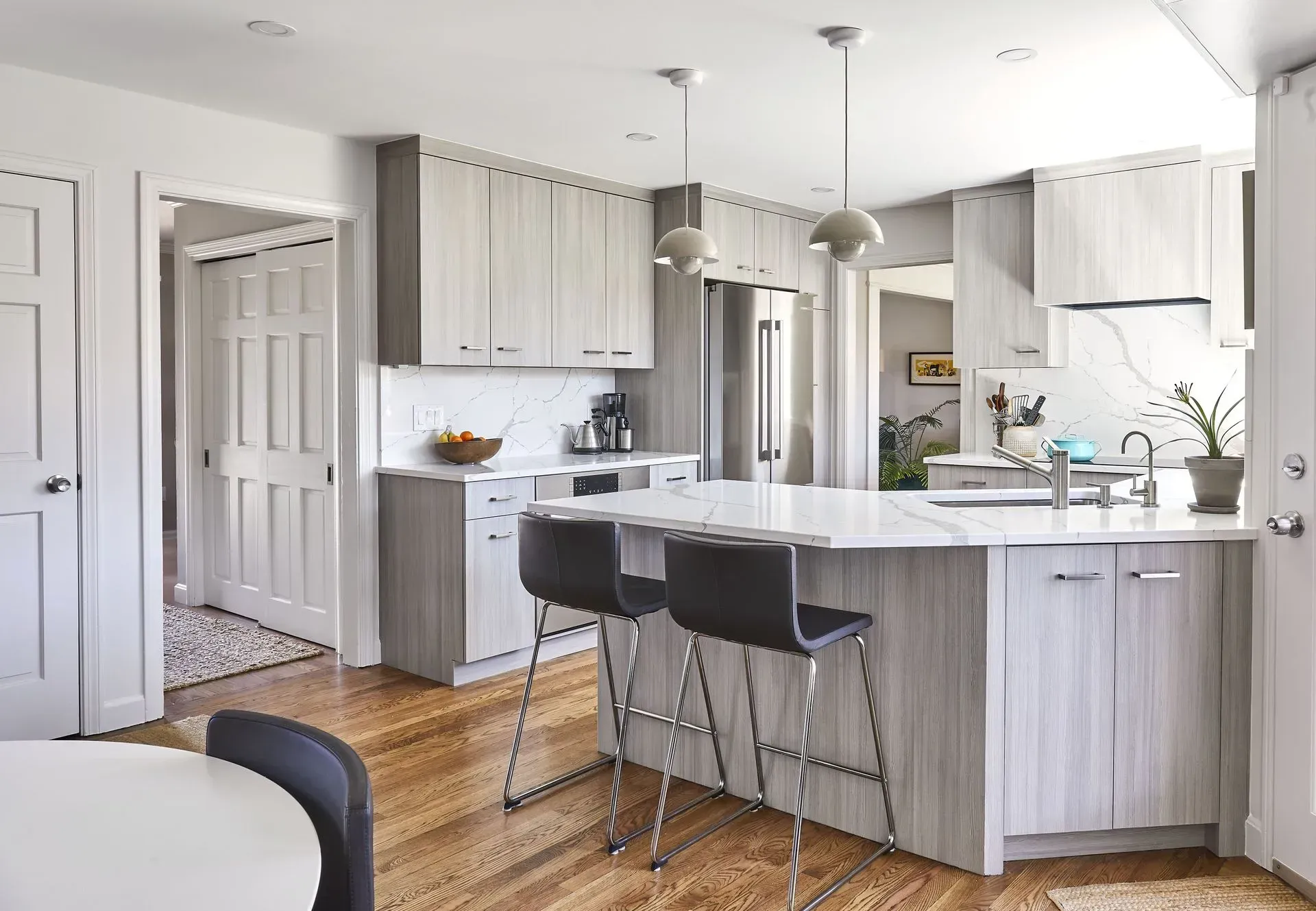 Modern kitchen with gray cabinets, white countertops, and wood floors. A kitchen island has three bar stools.