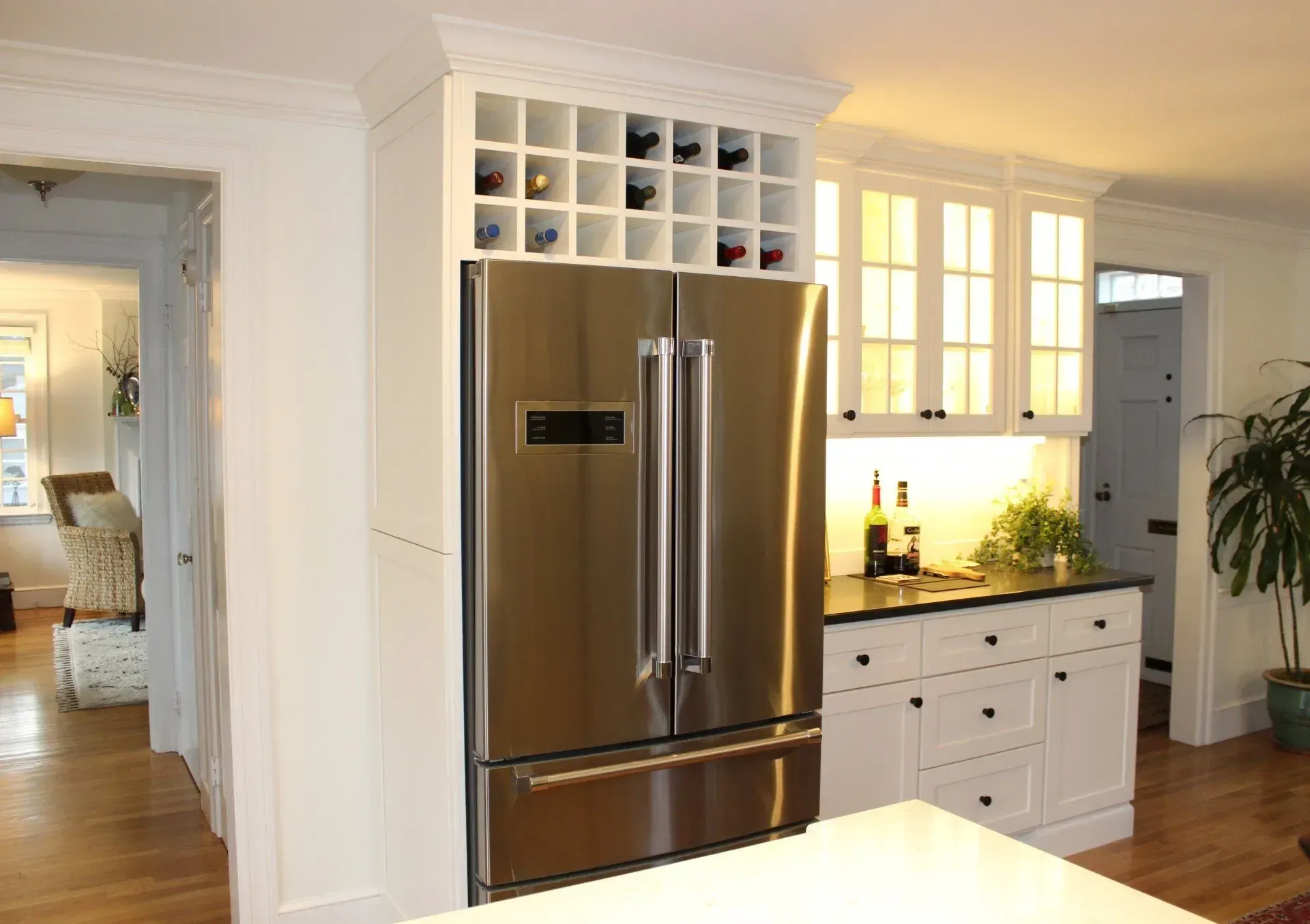 Stainless steel refrigerator built into white cabinetry with wine rack, in a kitchen.