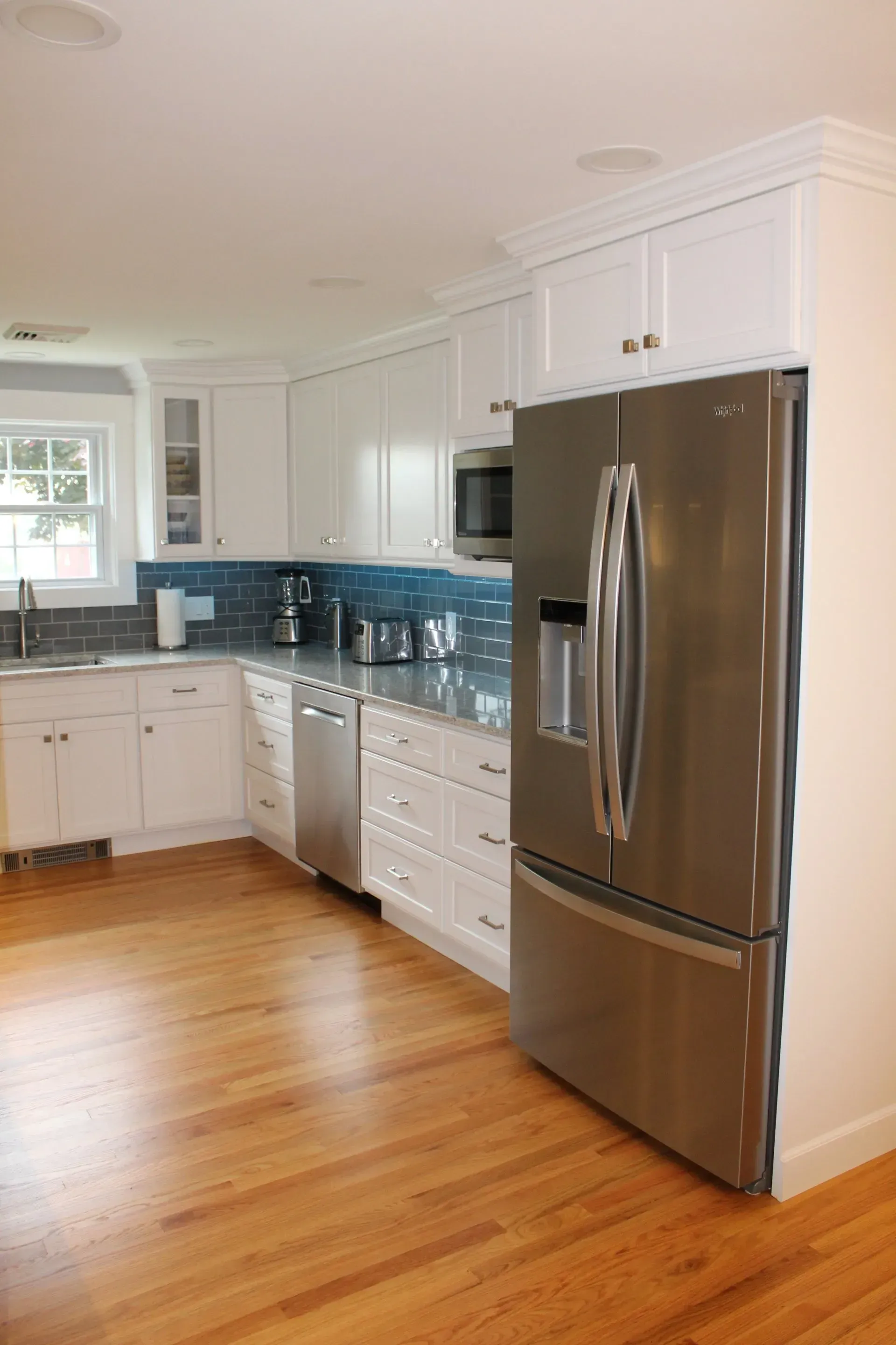 White kitchen with stainless steel appliances, blue backsplash, and light wood floors.