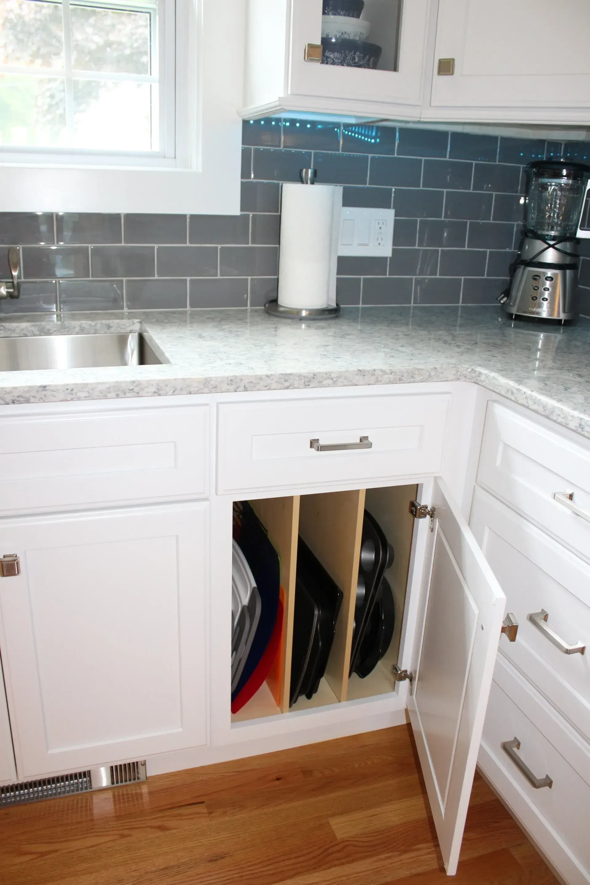 White kitchen cabinet with open door revealing vertical dividers holding baking pans.