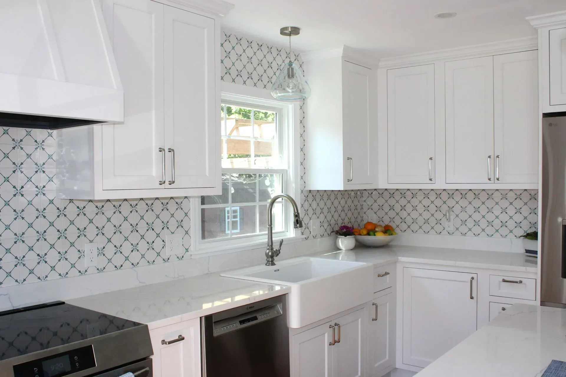 White kitchen with white cabinets, farmhouse sink, patterned backsplash, and stainless appliances.