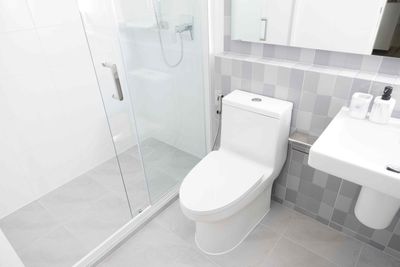 Brandon Handyman: A modern, minimalist white bathroom with a sink, toilet, and bidet, gray floor, and a radiator.