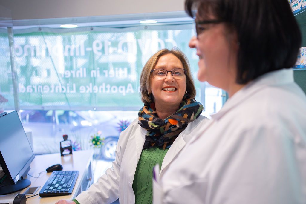Zwei Frauen in weißen Kitteln stehen nebeneinander in einer Apotheke.