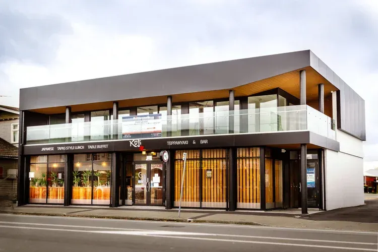 Modern two-story restaurant and bar with glass balcony. Black and white exterior, storefront with orange interior accents.