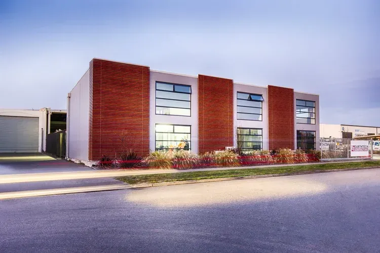 Modern two-story building with brick-like accents, large windows, and a blue sky background.