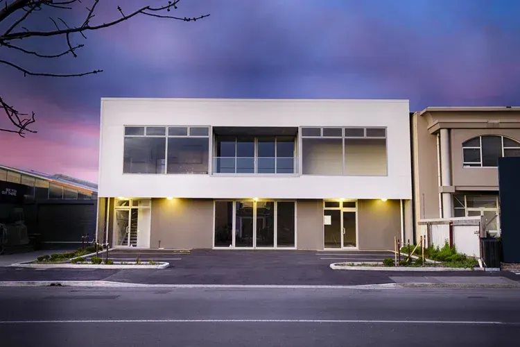 Modern white and grey commercial building with large windows, dark sky in background.