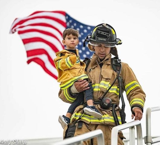 A fireman is carrying a little boy in front of an American flag