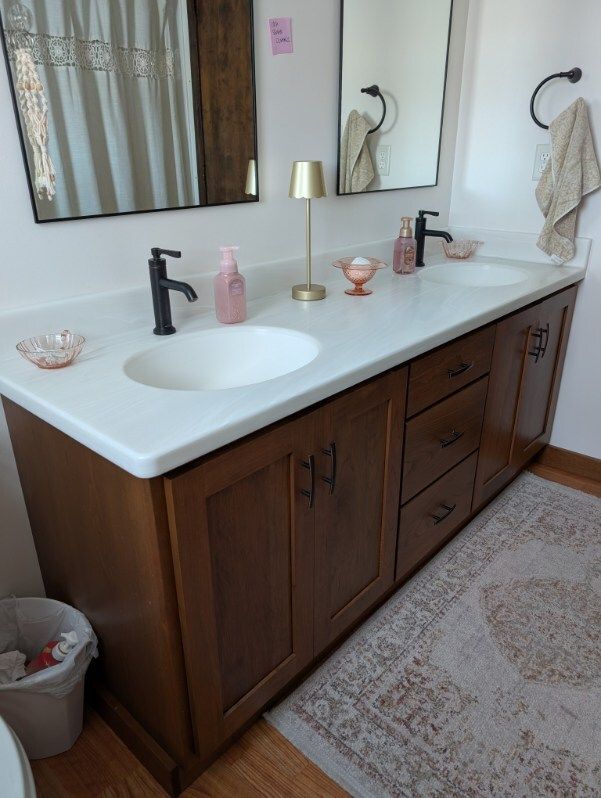 A bathroom vanity with a white countertop, two sinks, dark matte faucets, wood cabinets, and two mirrors on a white wall.