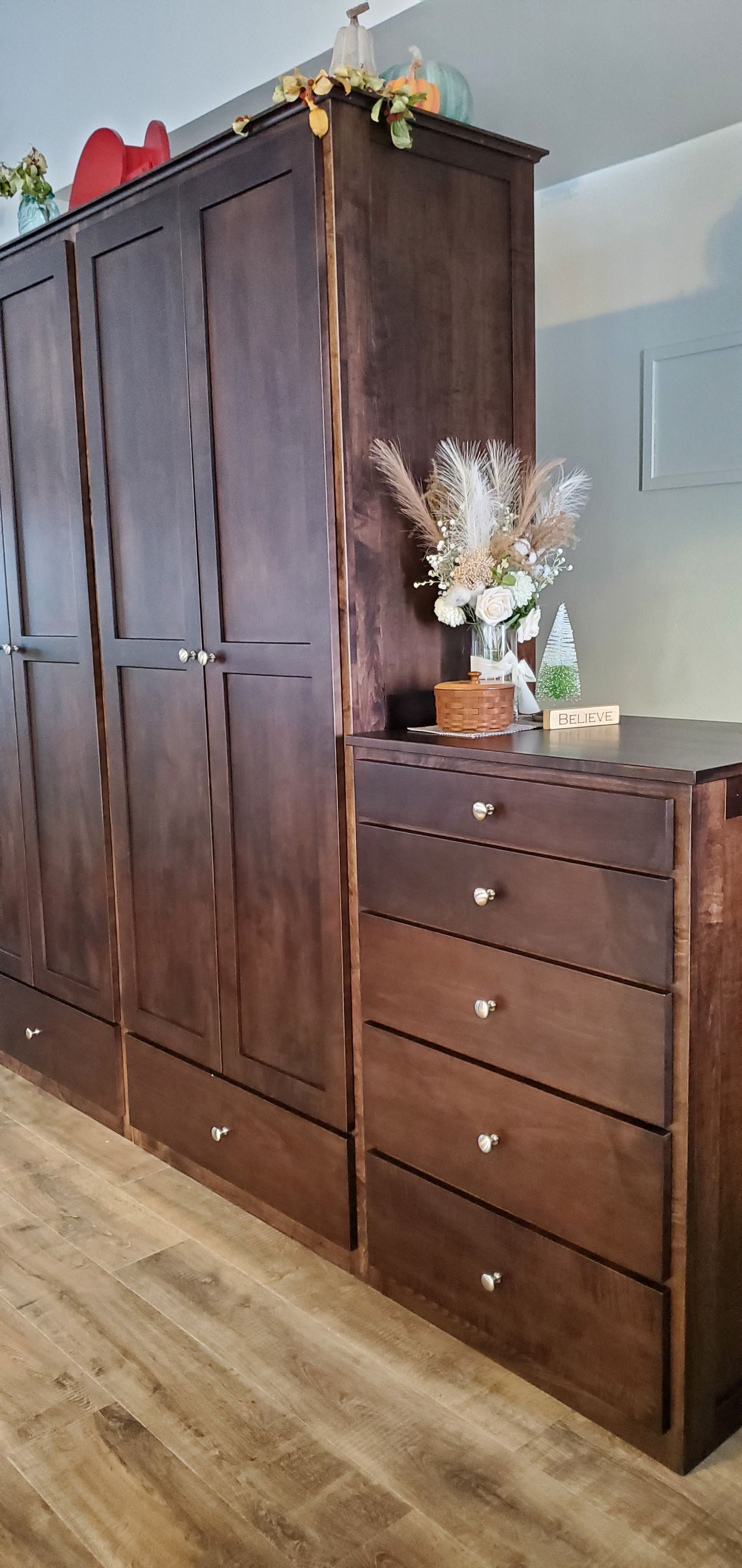 A tall dark-wood wardrobe paired with a matching five-drawer dresser, decorated with floral accents and a small pumpkin.