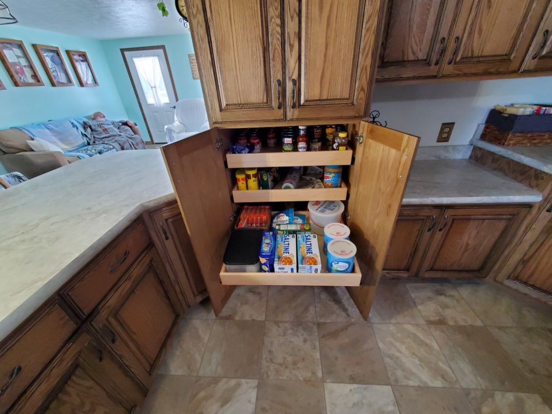 Open wooden pantry cabinet in a kitchen with three pull-out shelves filled with various food items.