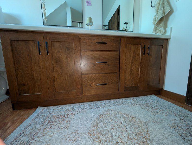 A bathroom vanity with dark wood cabinets and drawers, a light countertop, two mirrors, and a patterned rug on the floor.