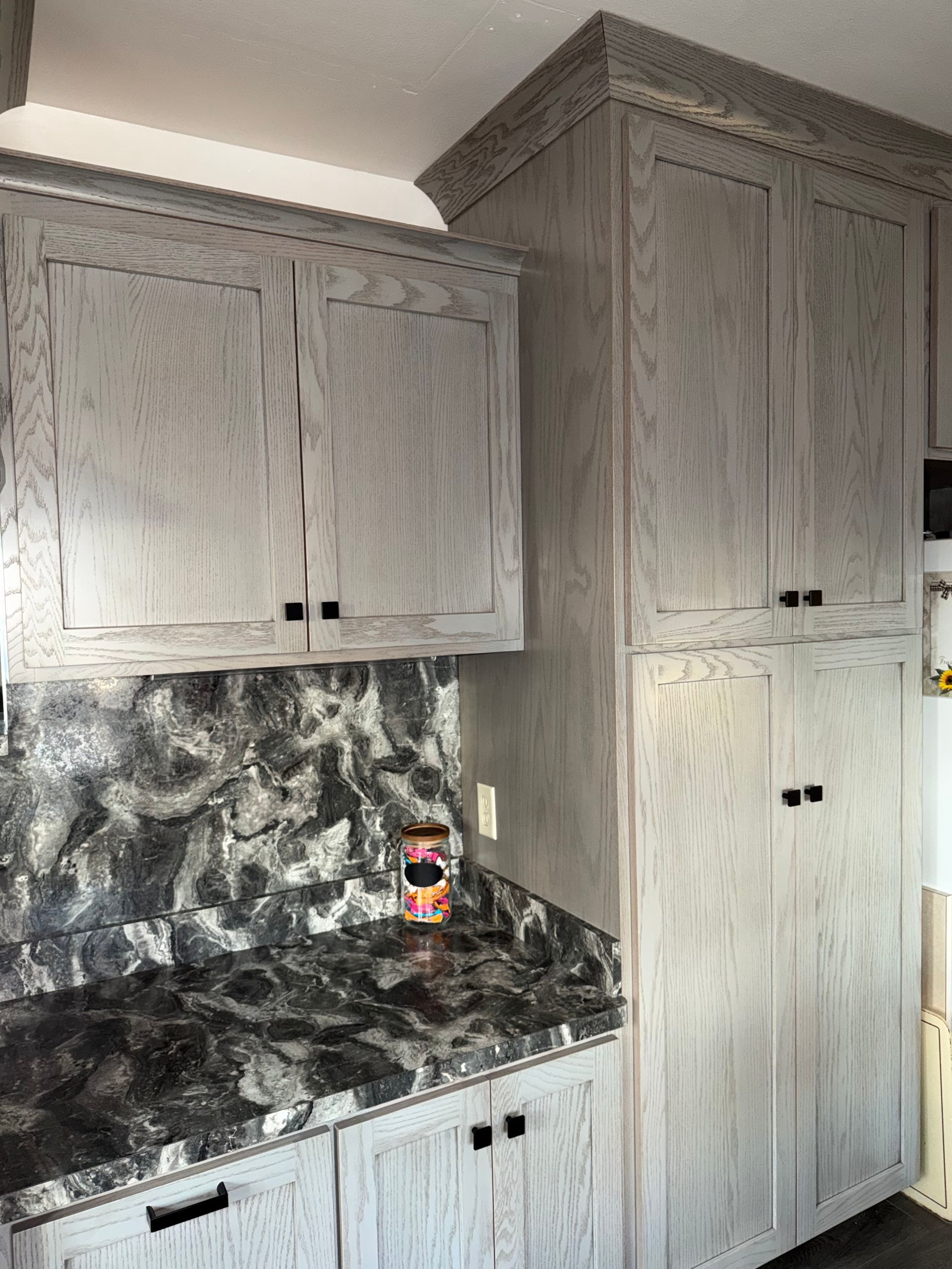 Gray wood-grain kitchen cabinets with dark, marbled countertops in a kitchen setting.