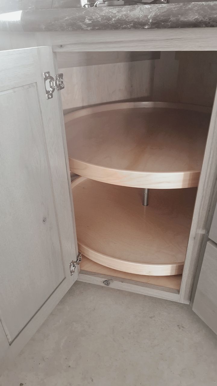 Open kitchen cabinet with two light wood circular rotating shelves, commonly known as a lazy Susan.
