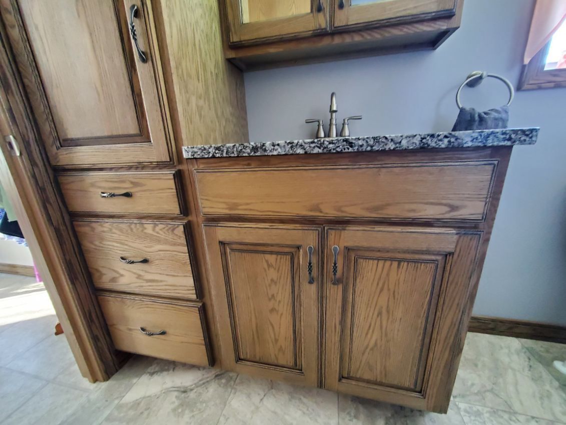 A bathroom vanity with oak cabinets, a granite countertop, sink faucet, and a wall-mounted towel ring.