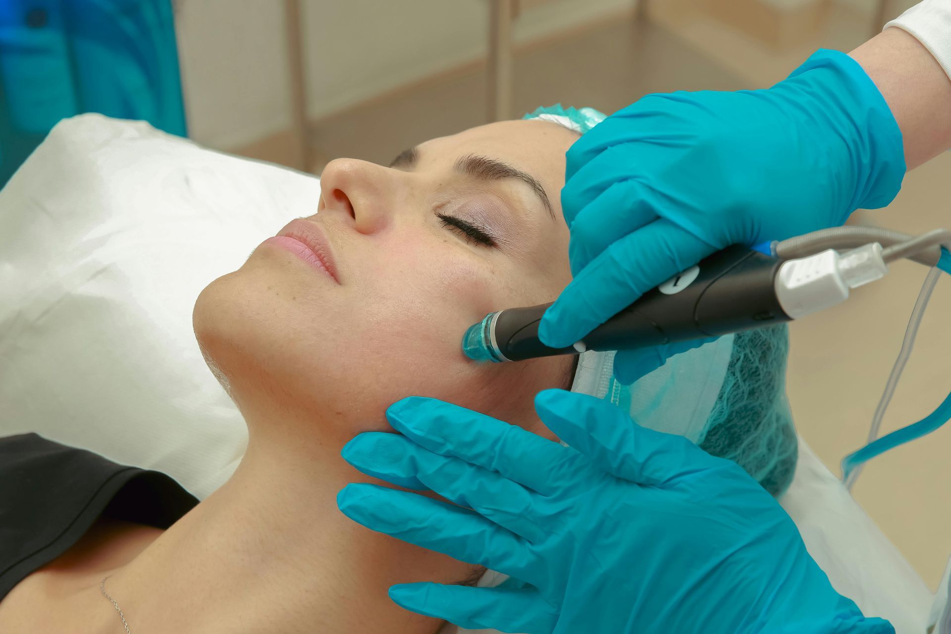 Gloved clinician applying facial treatment with a handheld device to a woman lying back on a treatment bed