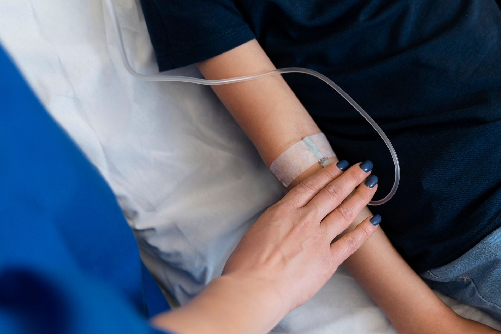 Hand resting on a patient’s arm with IV tubing in a hospital setting