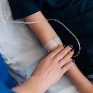 Hand resting on a patient’s arm with IV tubing in a hospital setting