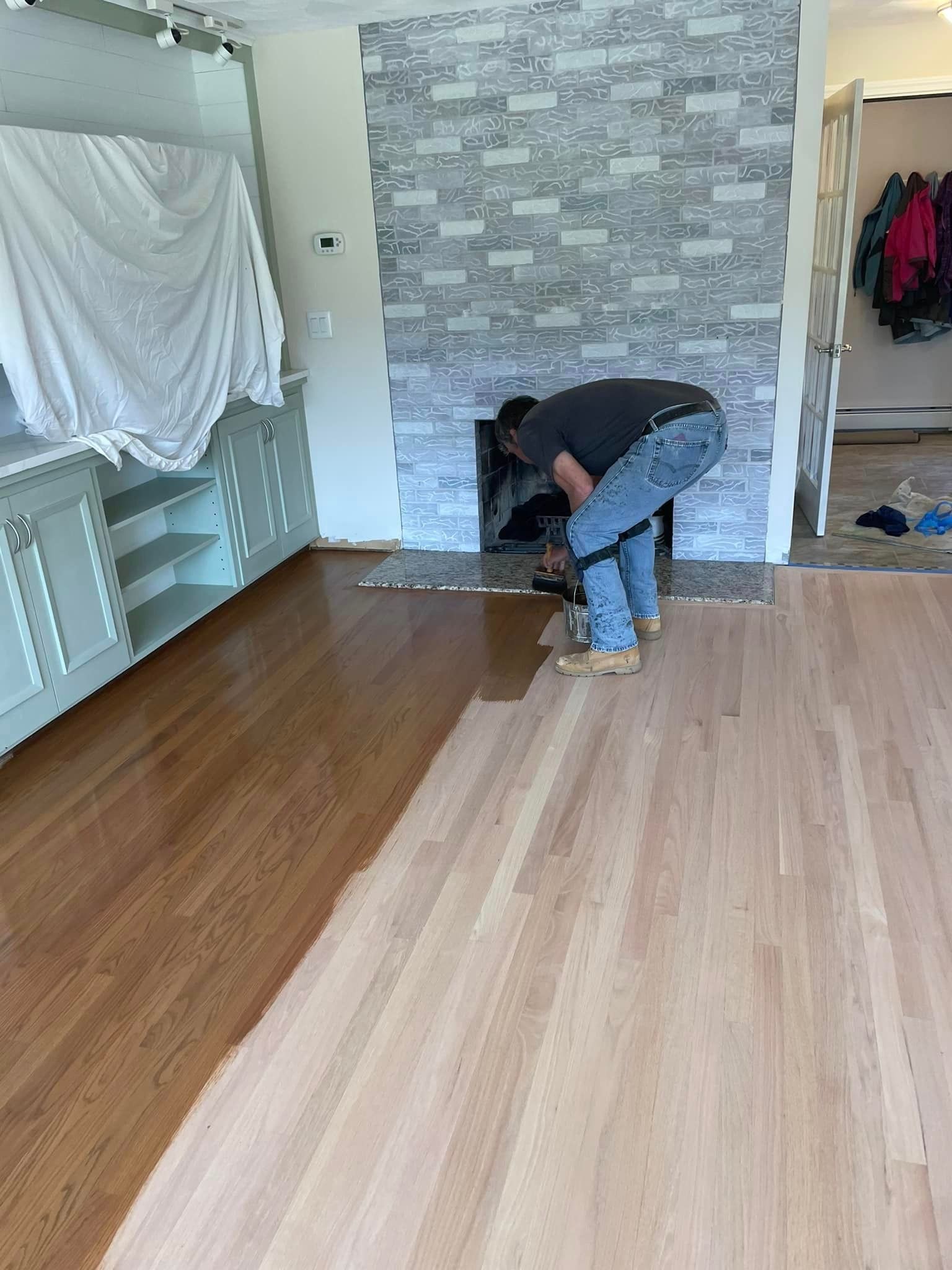A man is painting a wooden floor in a living room.