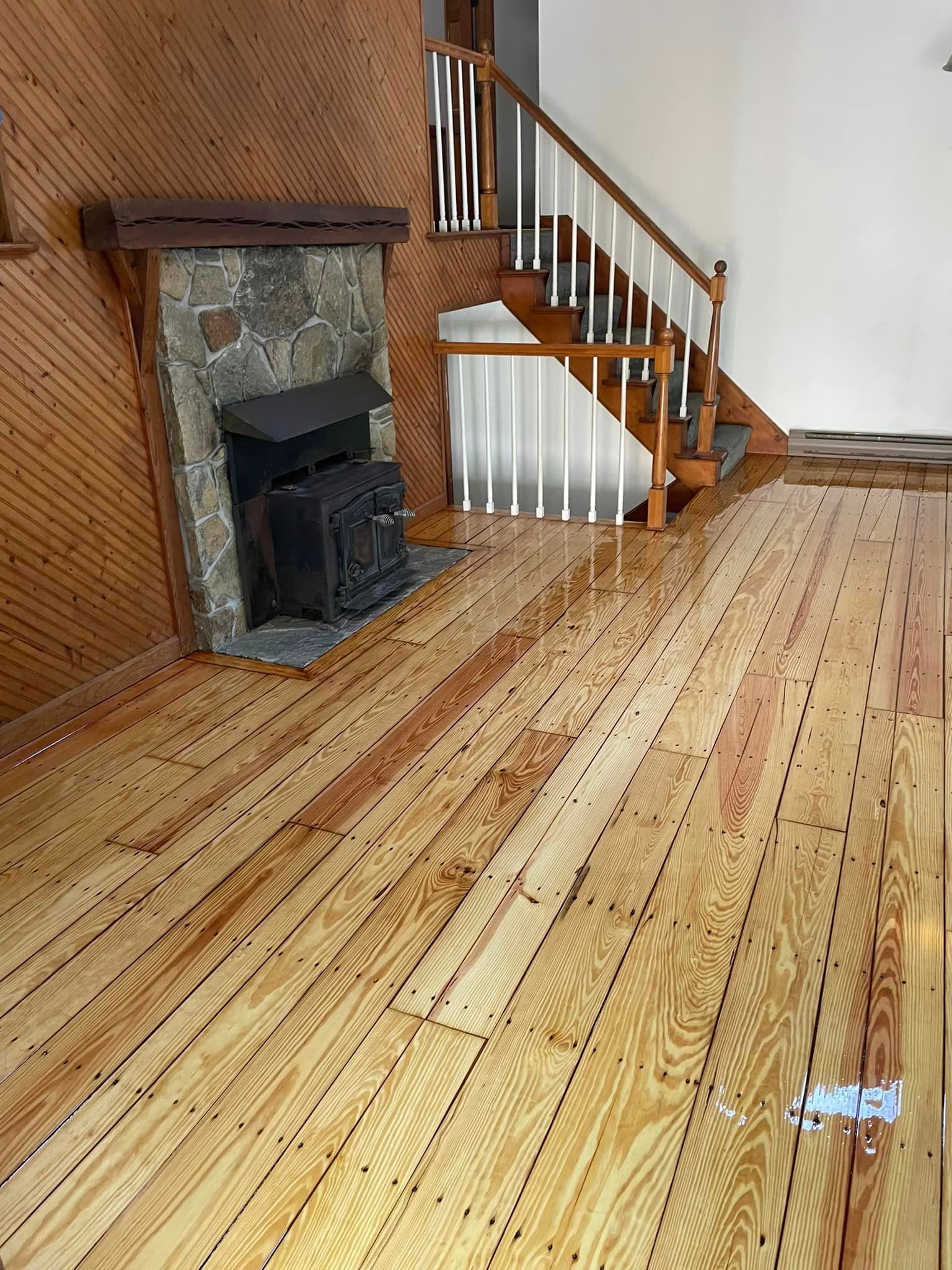 A wooden floor in a living room with stairs and a fireplace.