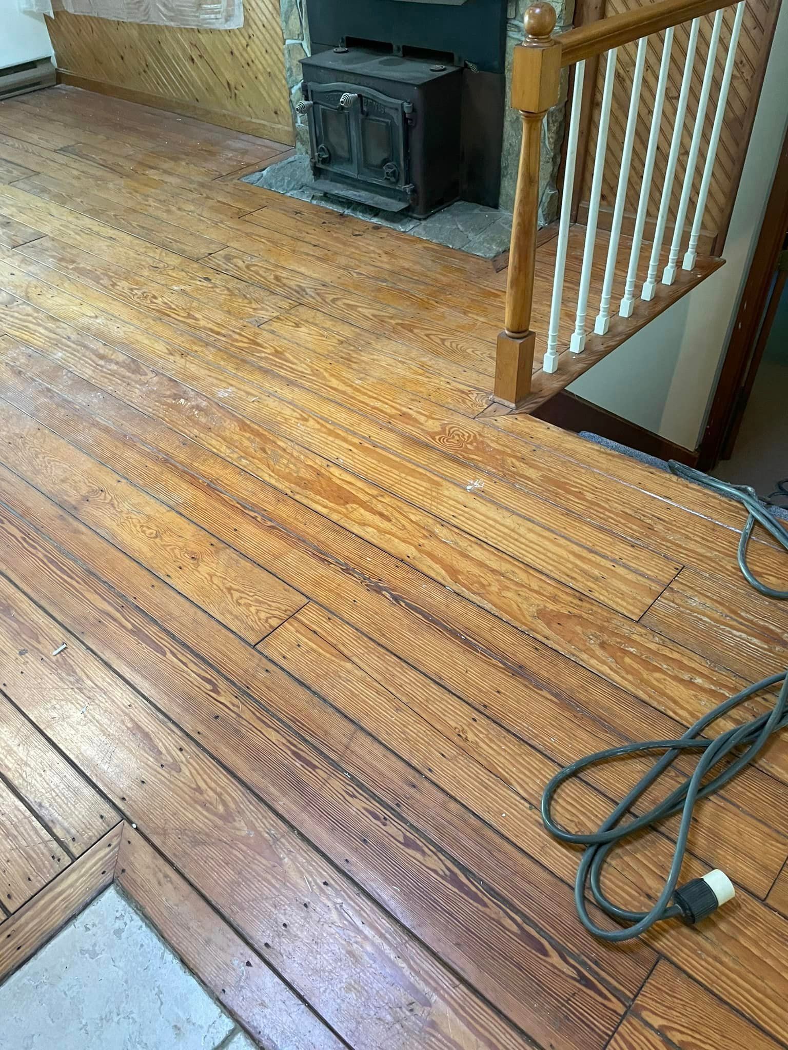A wooden floor with a fireplace and stairs in the background.