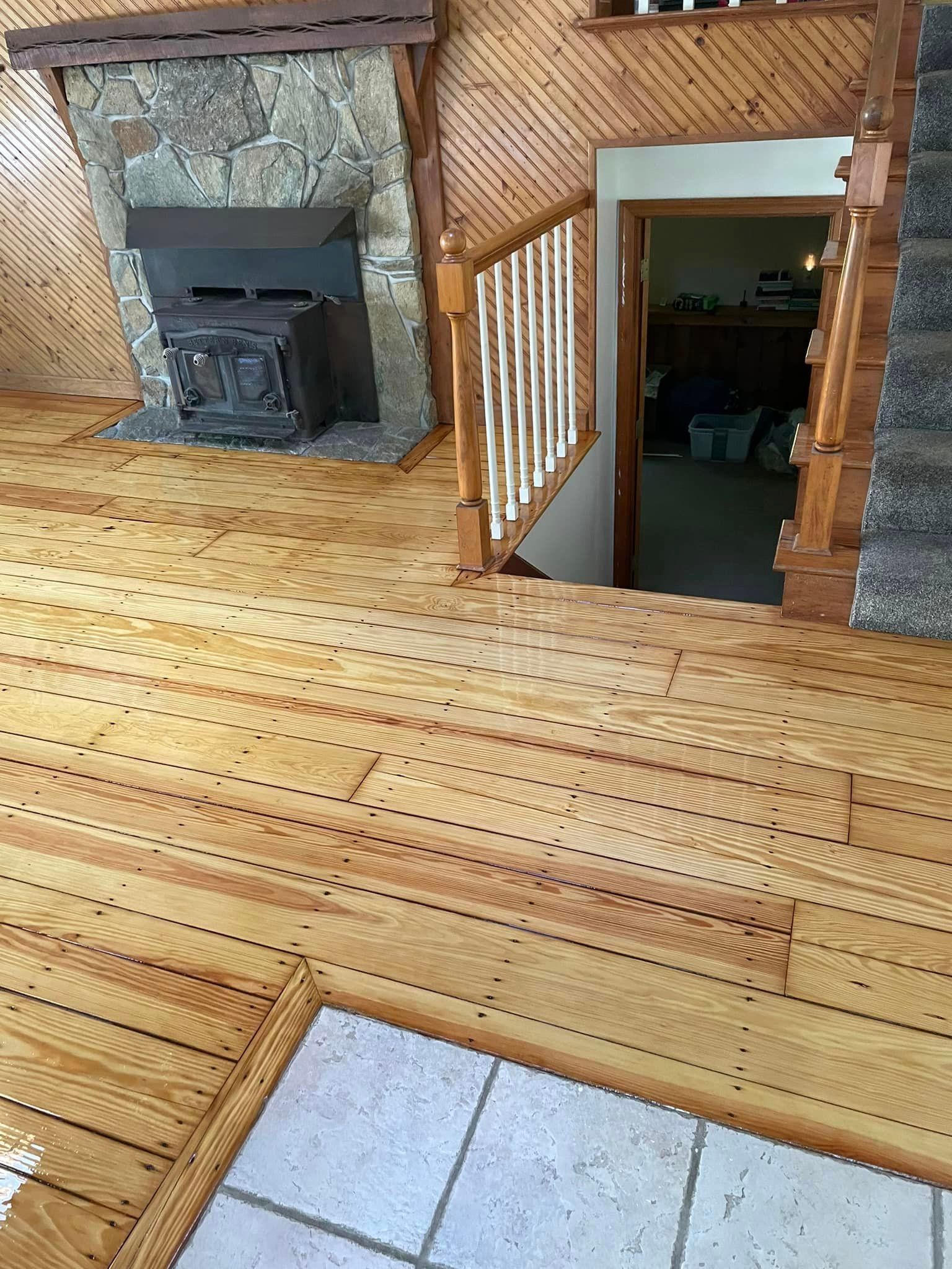 A wooden floor in a living room with a fireplace and stairs.