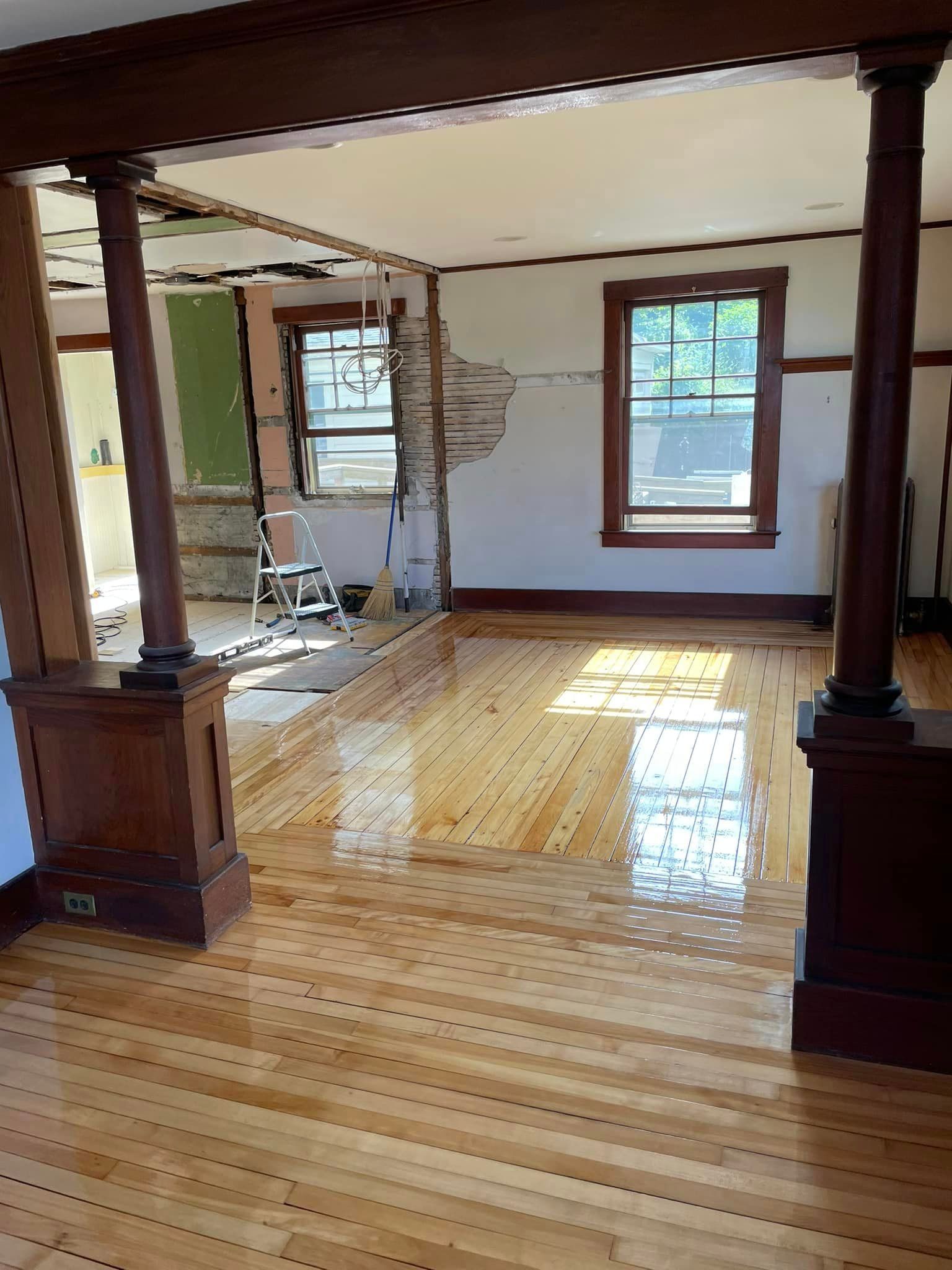 A living room with wooden floors and columns and a hole in the wall.