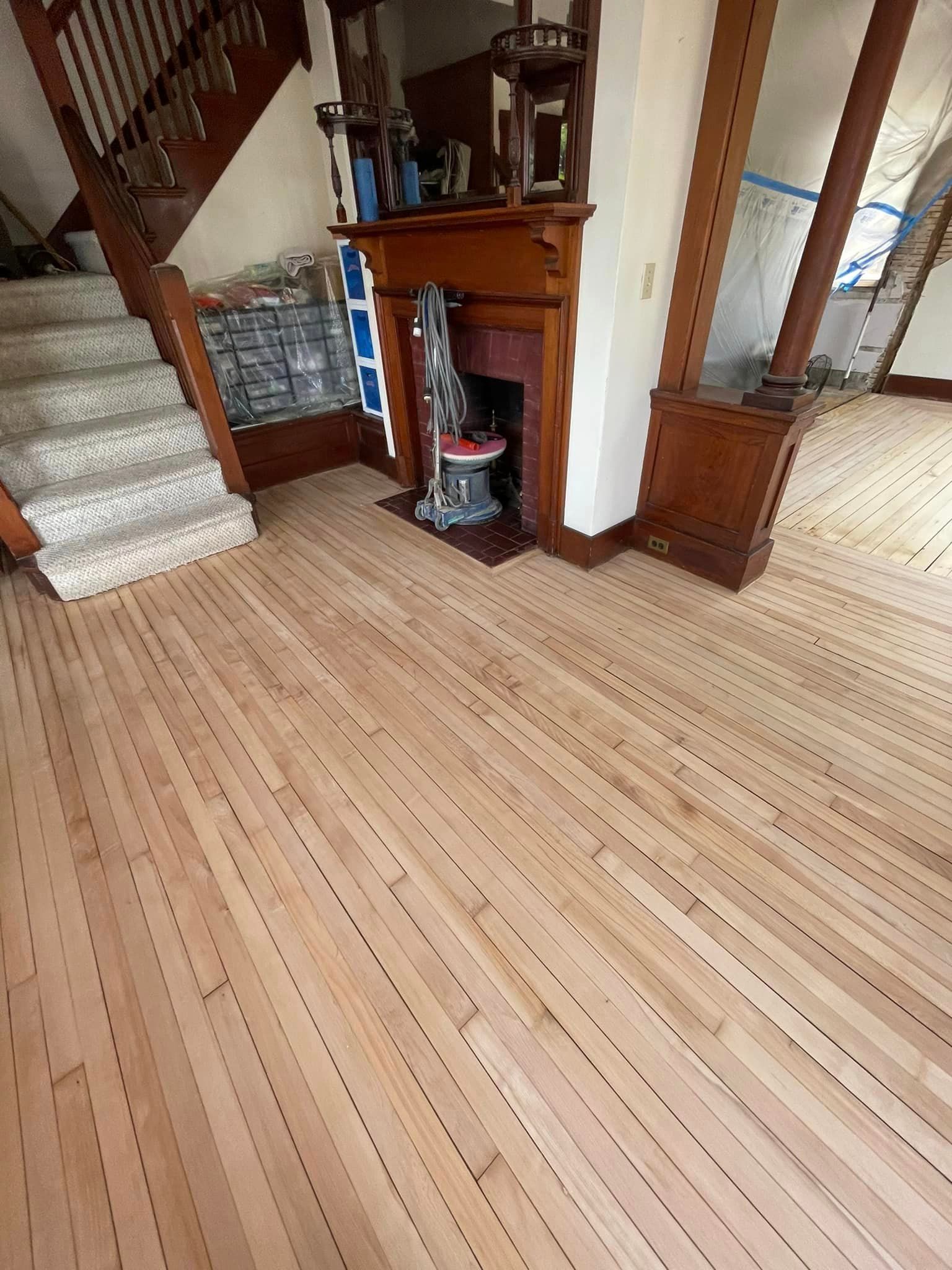 A wooden floor in a living room with a fireplace and stairs.