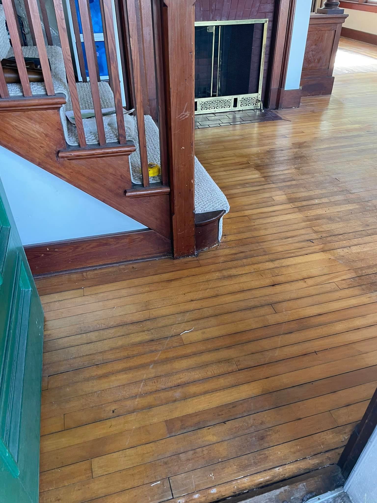 A wooden floor in a living room with stairs and a fireplace.